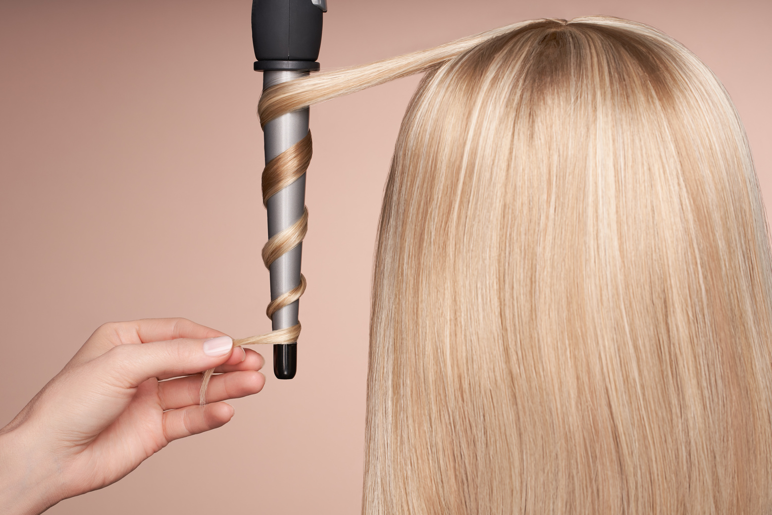 The hairdresser curls long hair with a Curling iron
